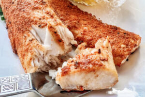 Two Mahi Mahi seasoned fillets on a white plate with a fork.