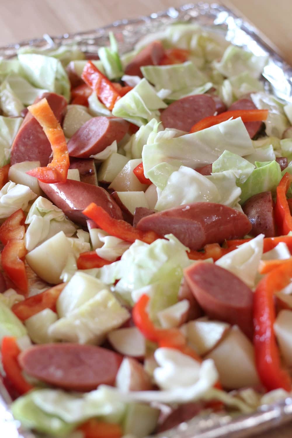 Sausage, cabbage, bell pepper and potatoes spread over a foil-lined baking sheet. 