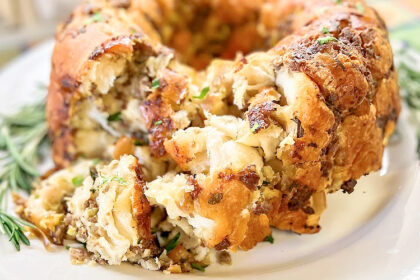 A ring of pull apart stuffing on a white serving platter with rosemary on the side.
