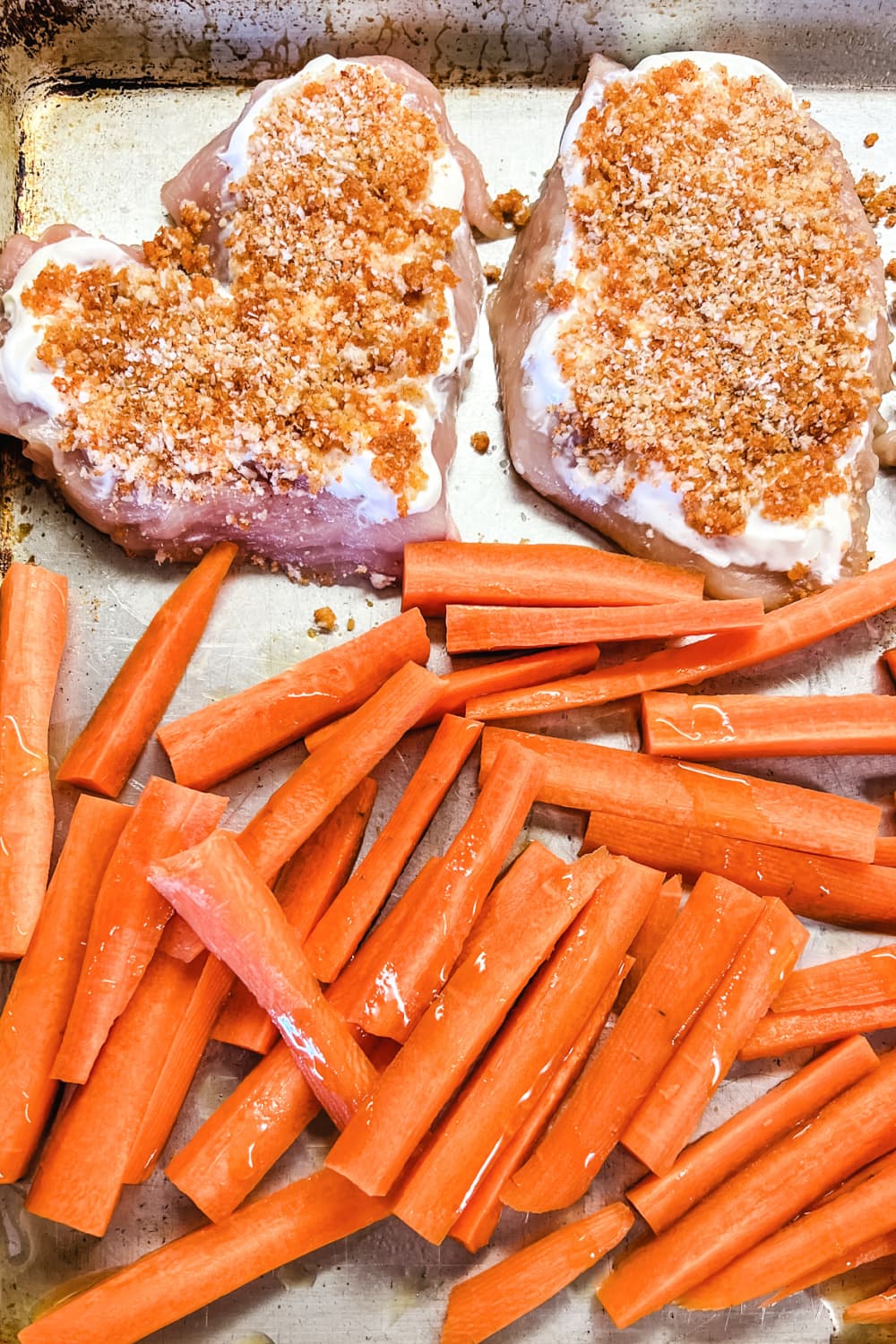 Crispy Parmesan Chicken Breasts with raw carrots on a baking sheet. 