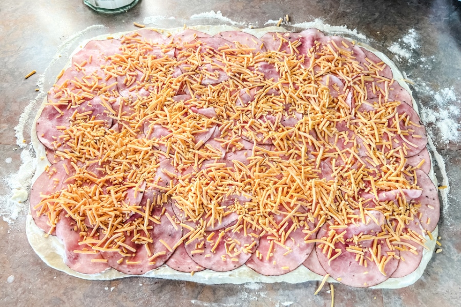 Cheese sprinkled over a layer of ham on bread dough.