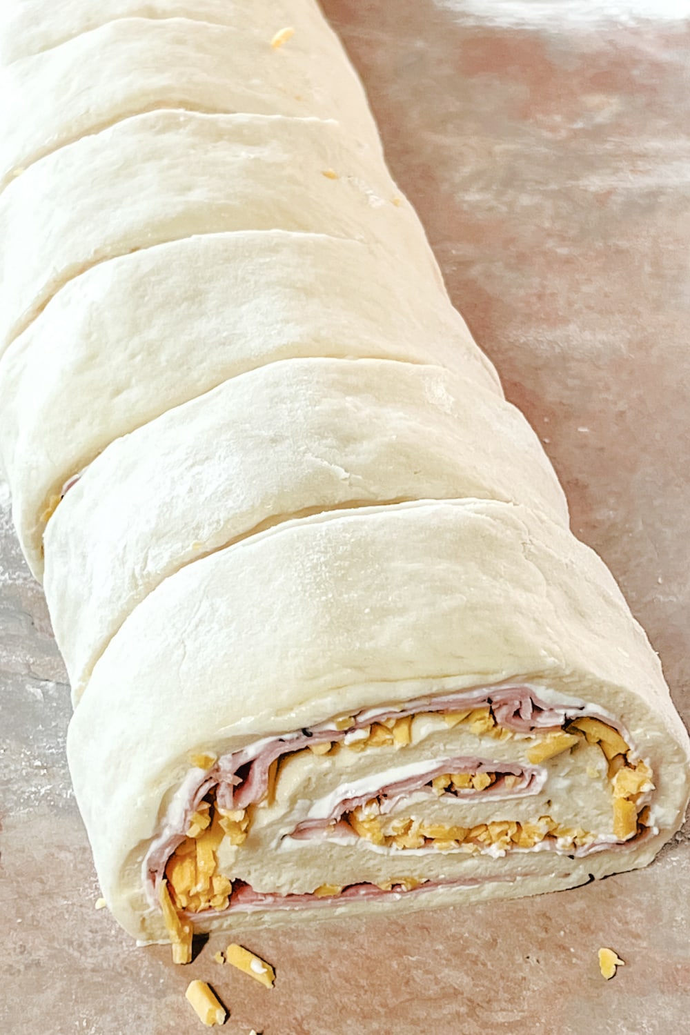 The log of dough with ham and cheese filling sliced into rolls.