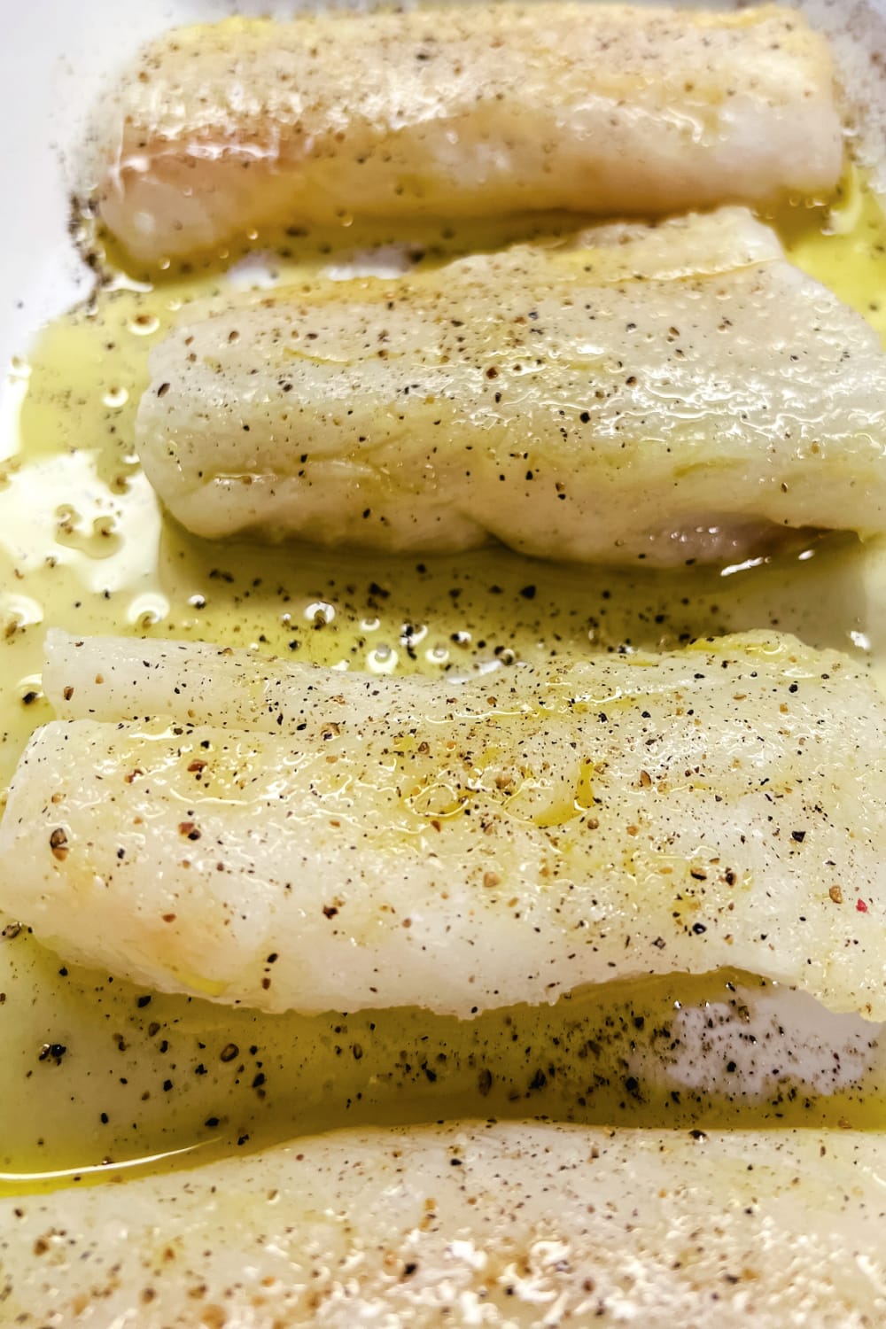 Seasoned cod fillets in a white baking dish. 