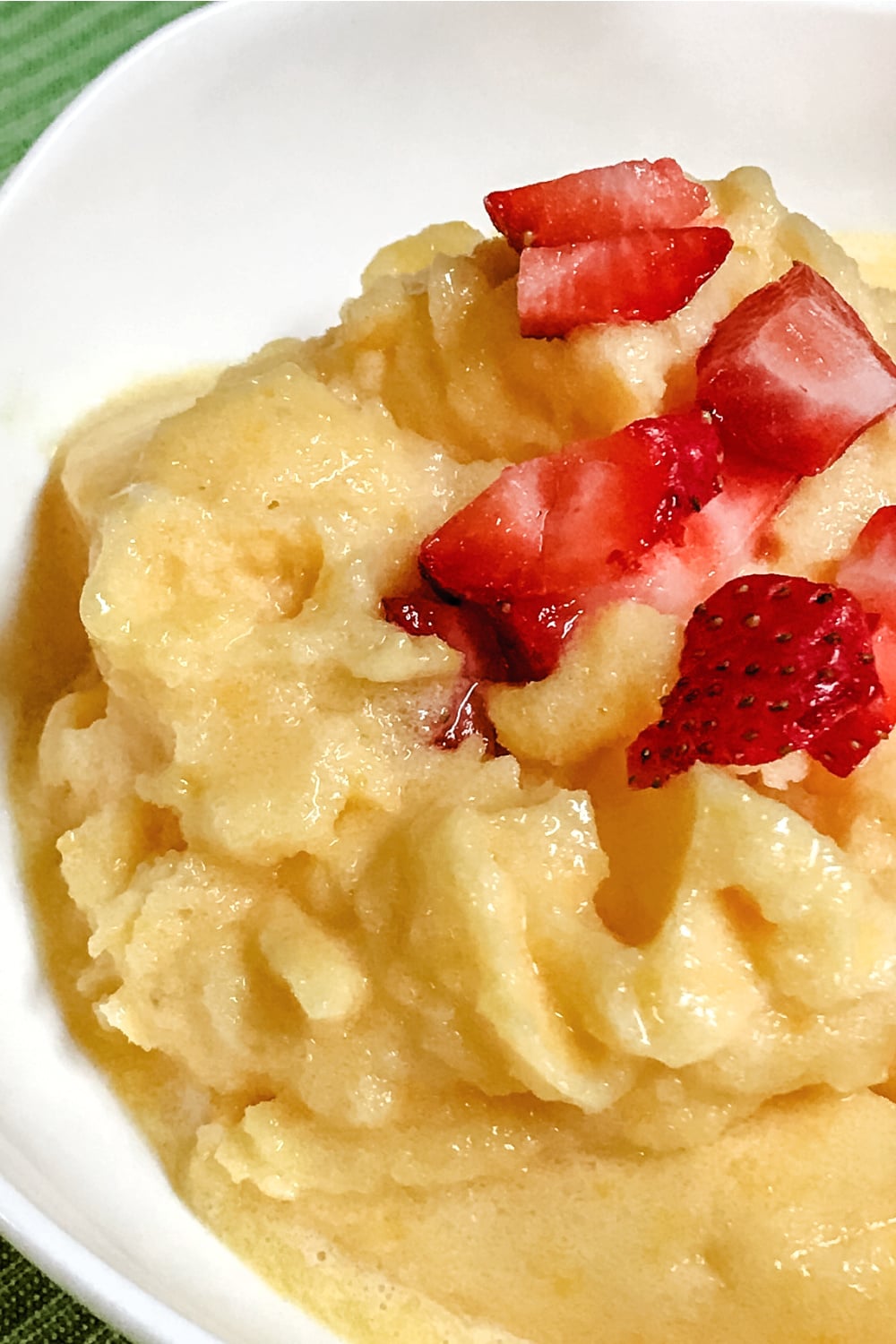 Frozen mango sorbet in a white bowl, topped with strawberries. 