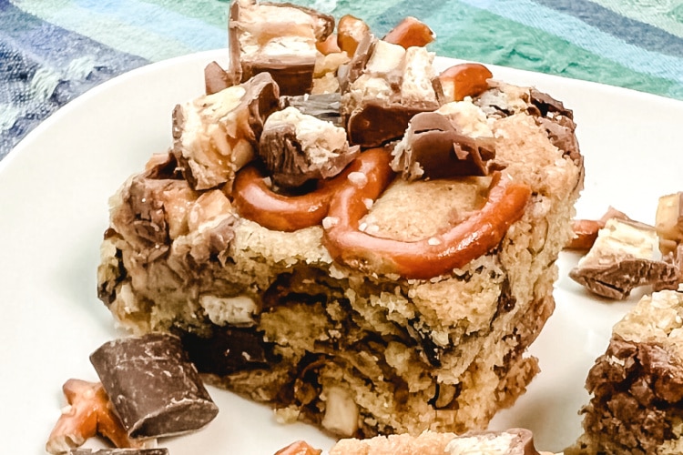 A square of Chocolate Chunk Snickers Bar Cookies on a white plate.