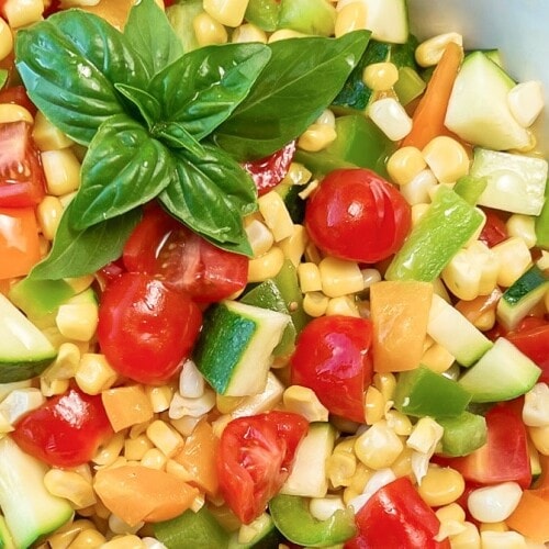 A large bowl of corn salad garnished with basil sprigs.