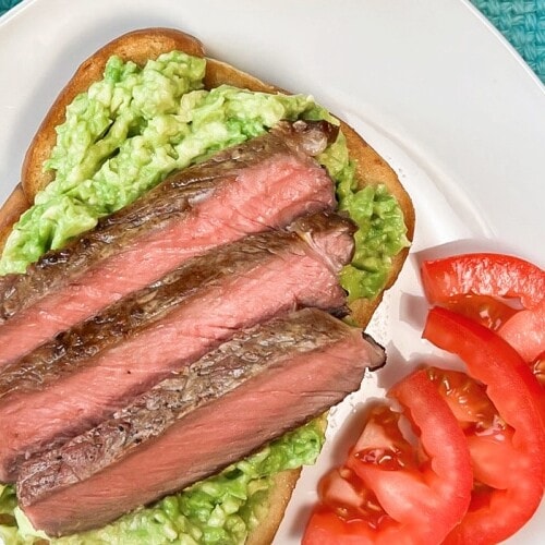 Medium-rare slices of rib eye steak on a bed of mashed avocados.