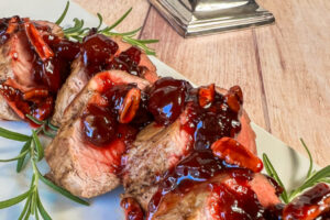 Slabs of pork tenderloin overlapped on top of each other with cherry sauce over all.