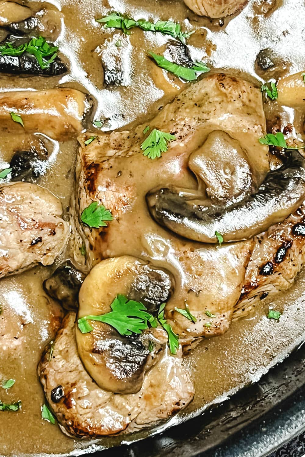 A saute pan full of sizzle steaks in mushroom gravy garnished with fresh parsley. 
