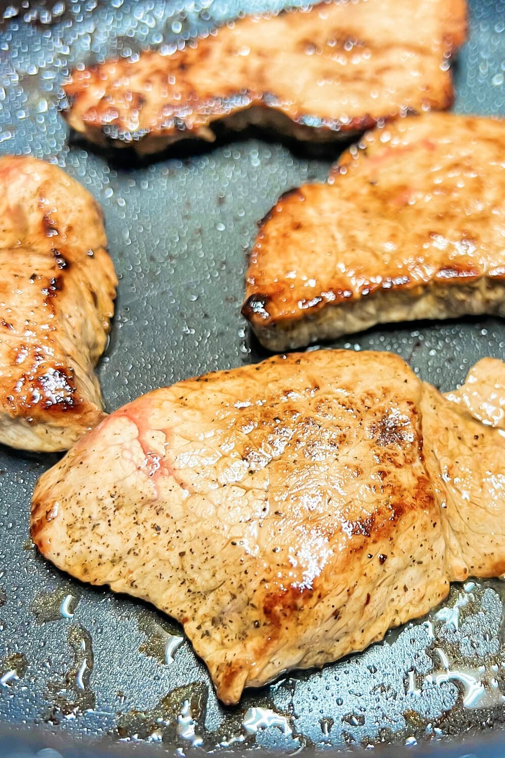 A pan full of sizzling steaks that are caramelized. 