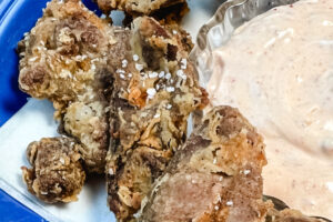 Golden brown fried chicken gizzards with dipping sauce on the side.