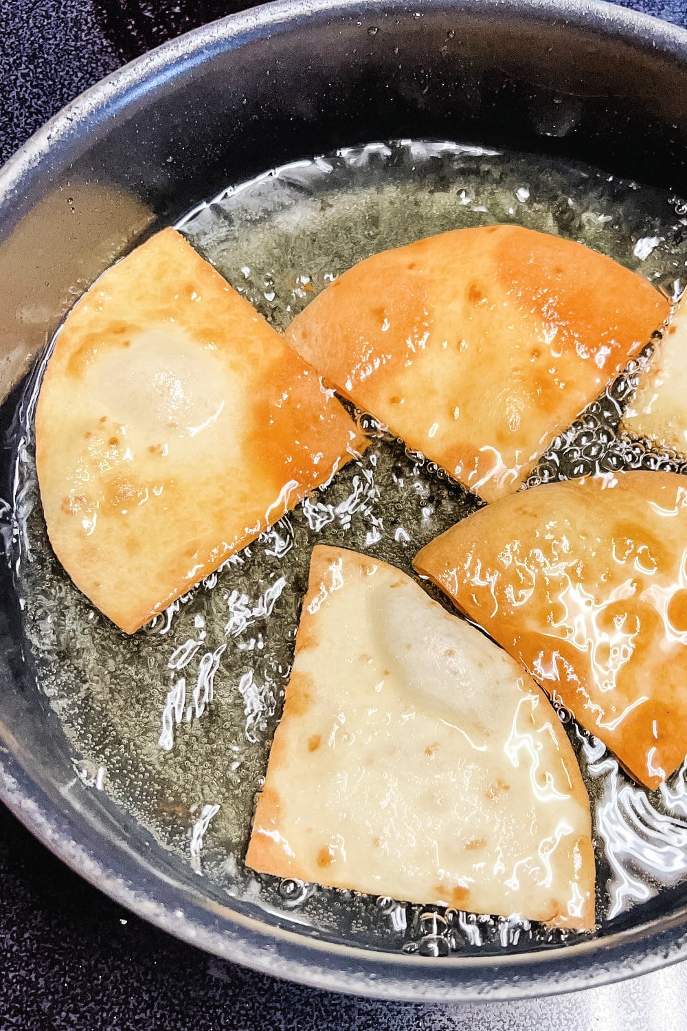 Flour tortilla triangles frying in hot oil until golden brown. 