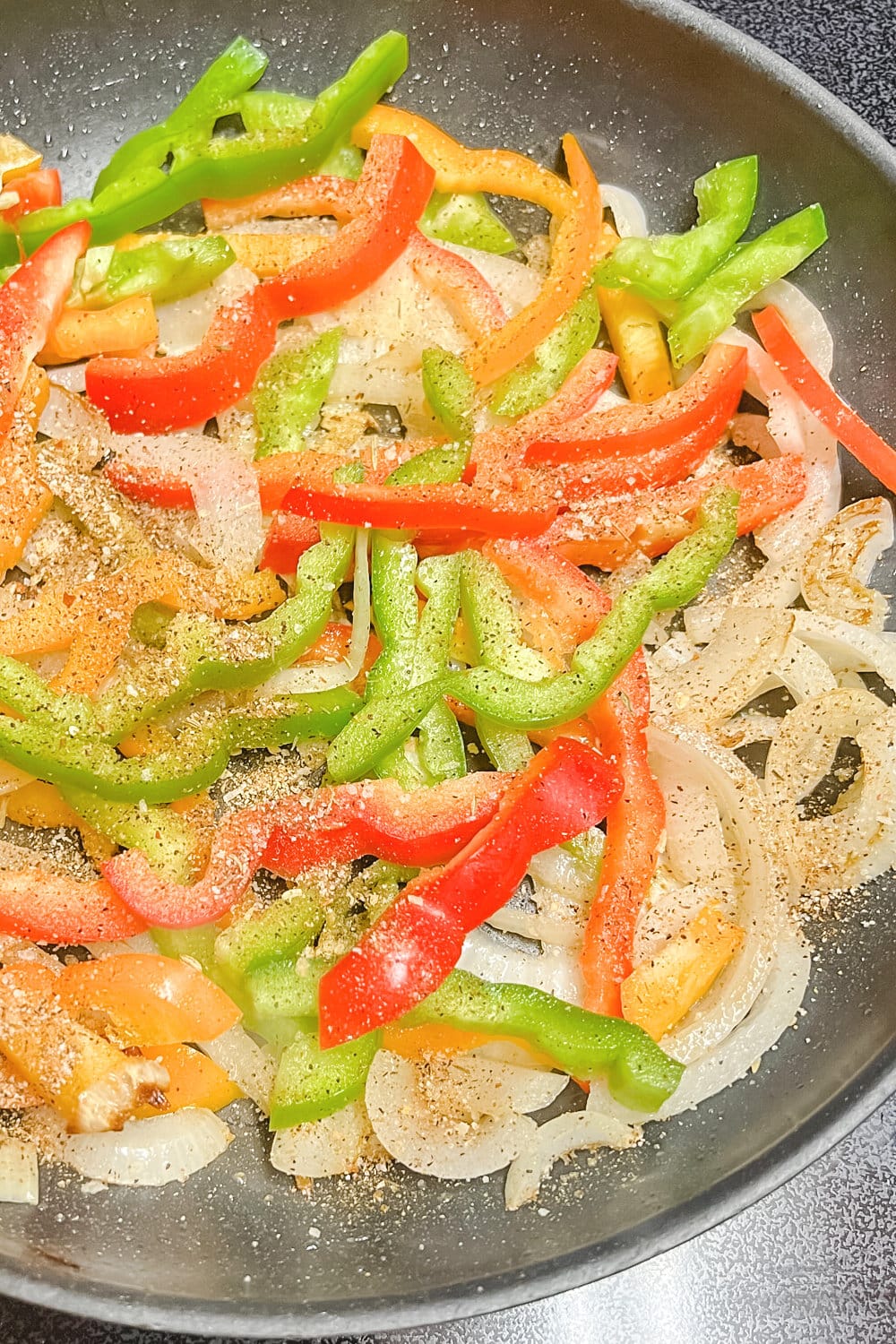 Sliced peppers and onions in a skillet. 