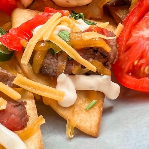 Beef Sizzle Steak Nachos with sour cream and sliced tomatoes.