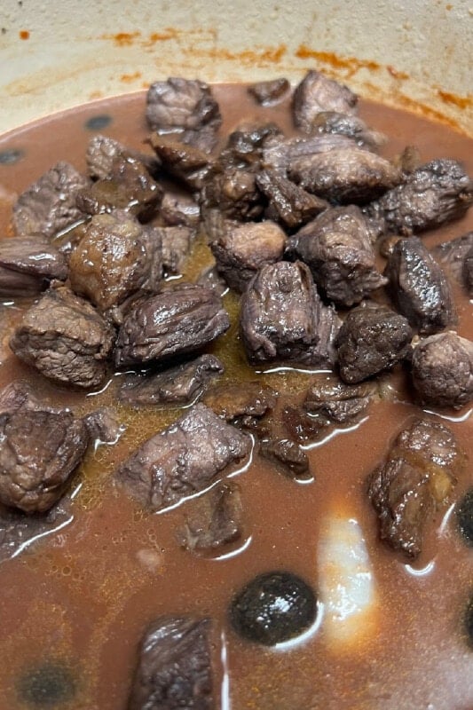 Browned beef stew meat added to the stew ingredients in the pot.