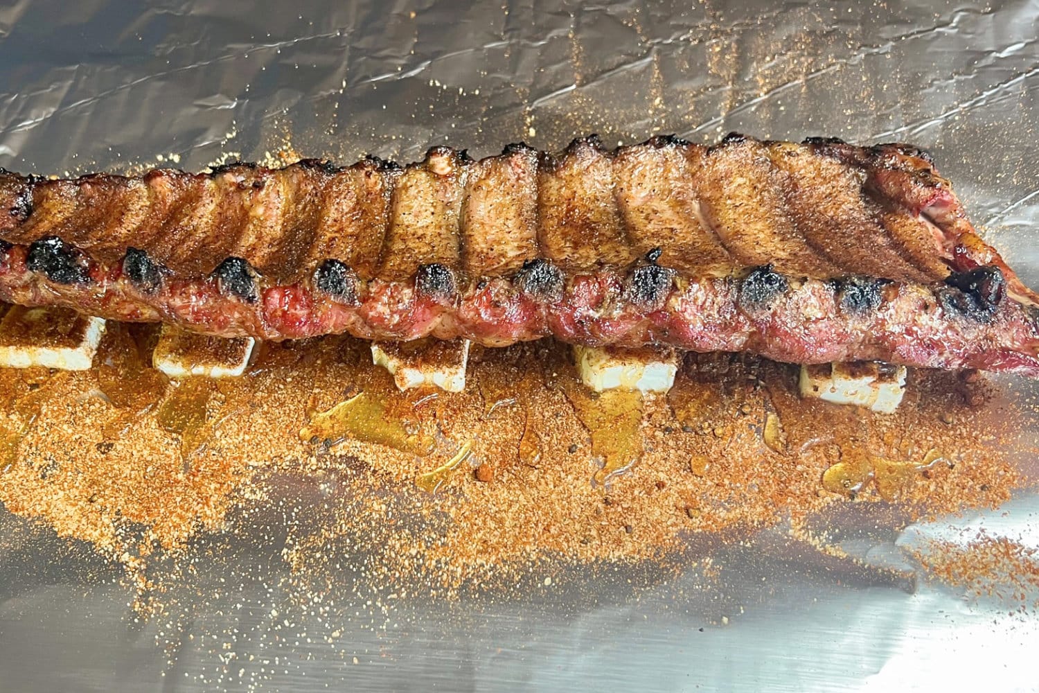 A rack of ribs placed onto butter, rib rub and honey, ready to be wrapped. 