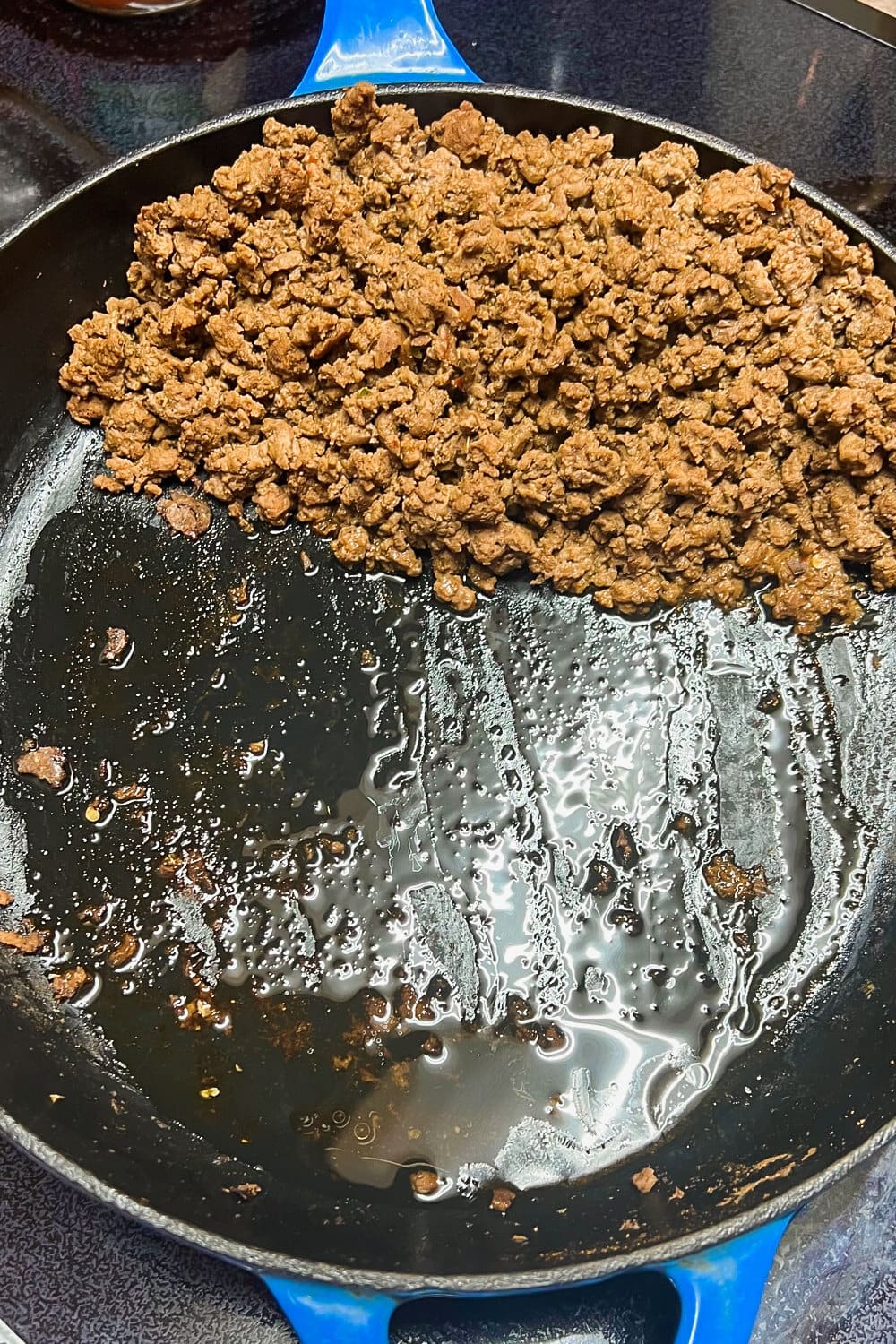 Cooked ground beef in a skillet with the fats draining to one side. 