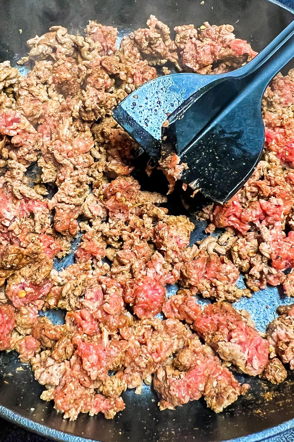 Crumbled ground beef cooking in a skillet. 