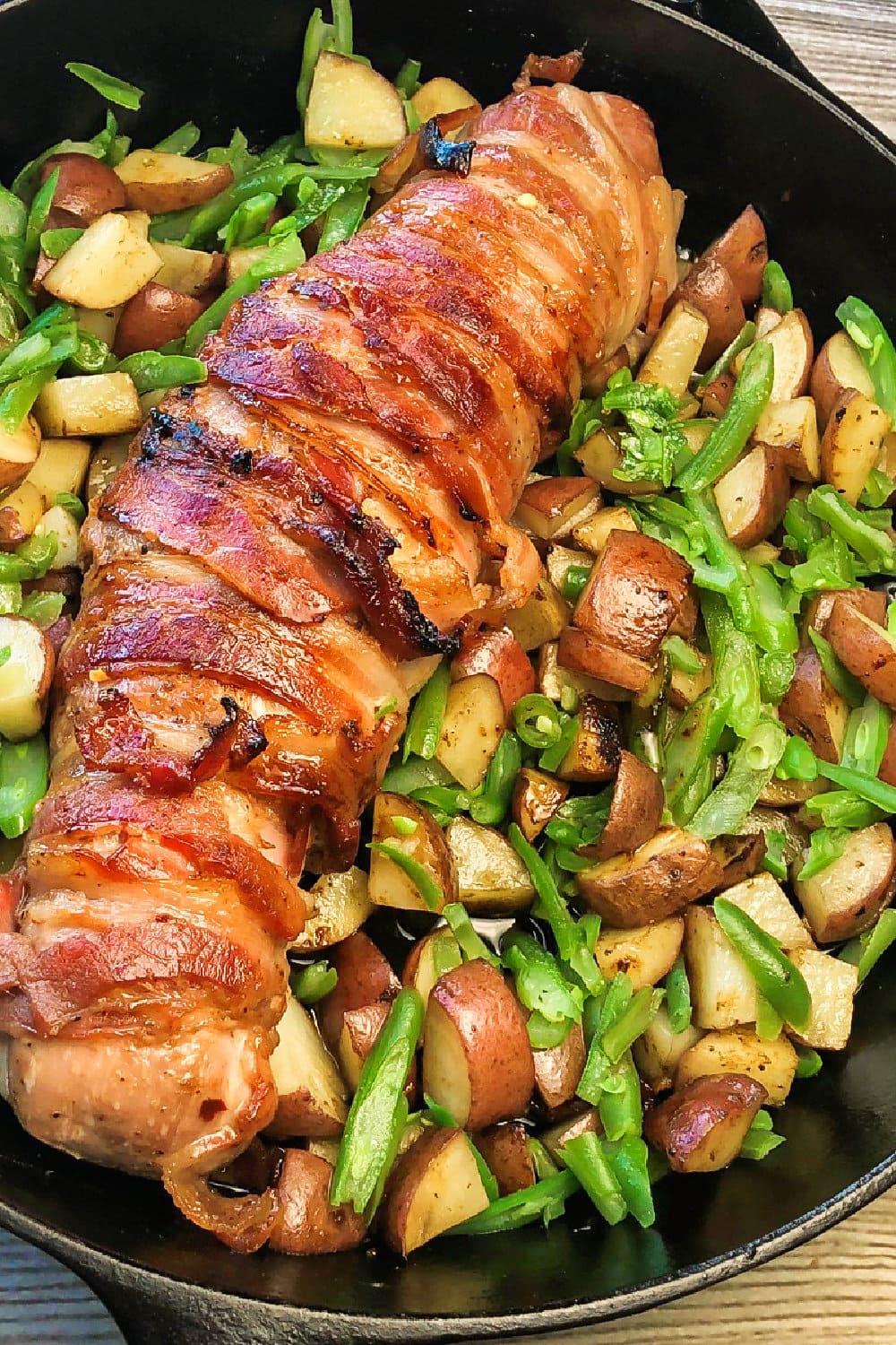 Bacon-wrapped roast pork tenderloin surrounded with veggies, ready to be served. 