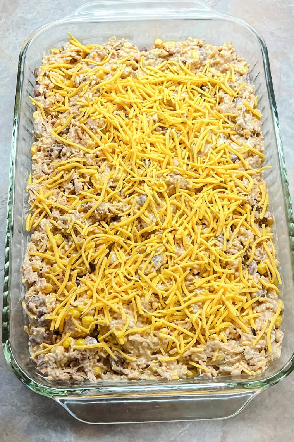 Taco Rice Casserole with shredded cheese on top, ready to bake. 