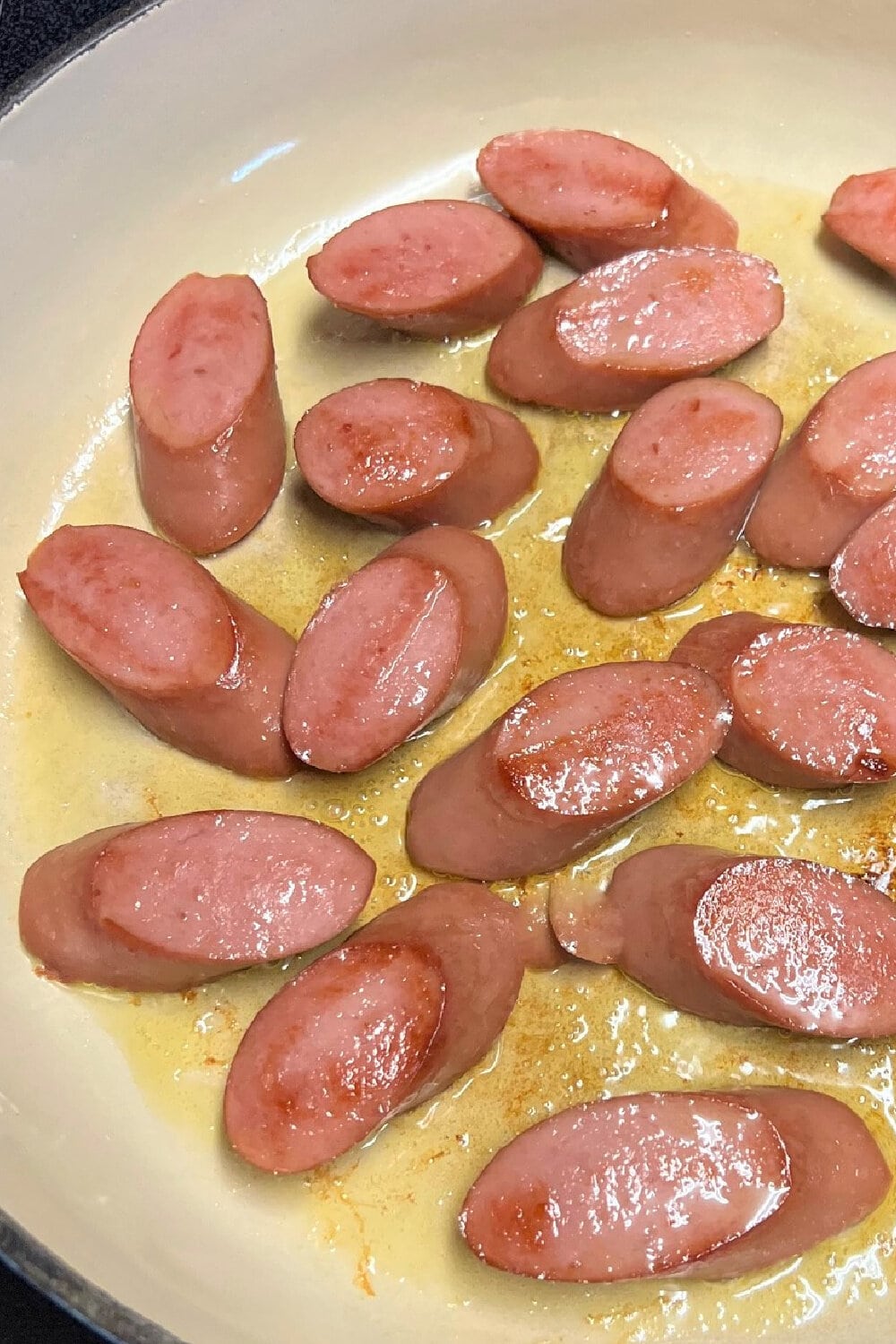 Slices of Kielbasa sausage, browning in hot oil. 