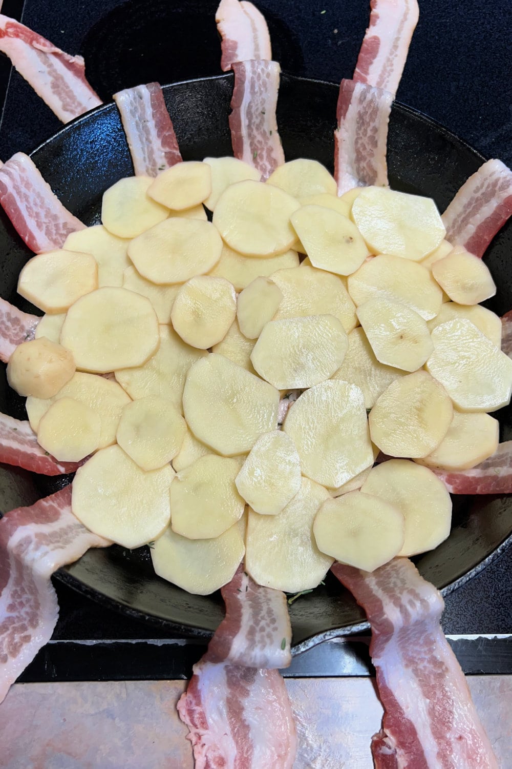 Sliced potatoes on top of bacon sliced in a skillet. 