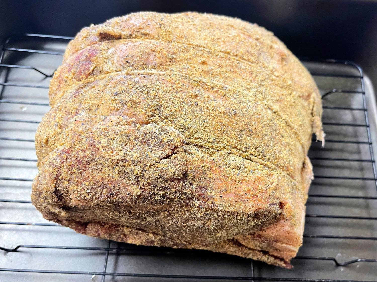 A seasoned prime rib roast on a rack in a roasting pan. 