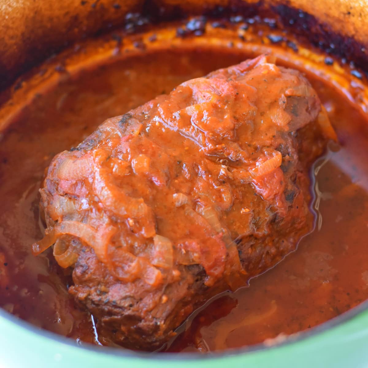 A tomato based sauce over a beef bottom round roast in a pot from the oven.