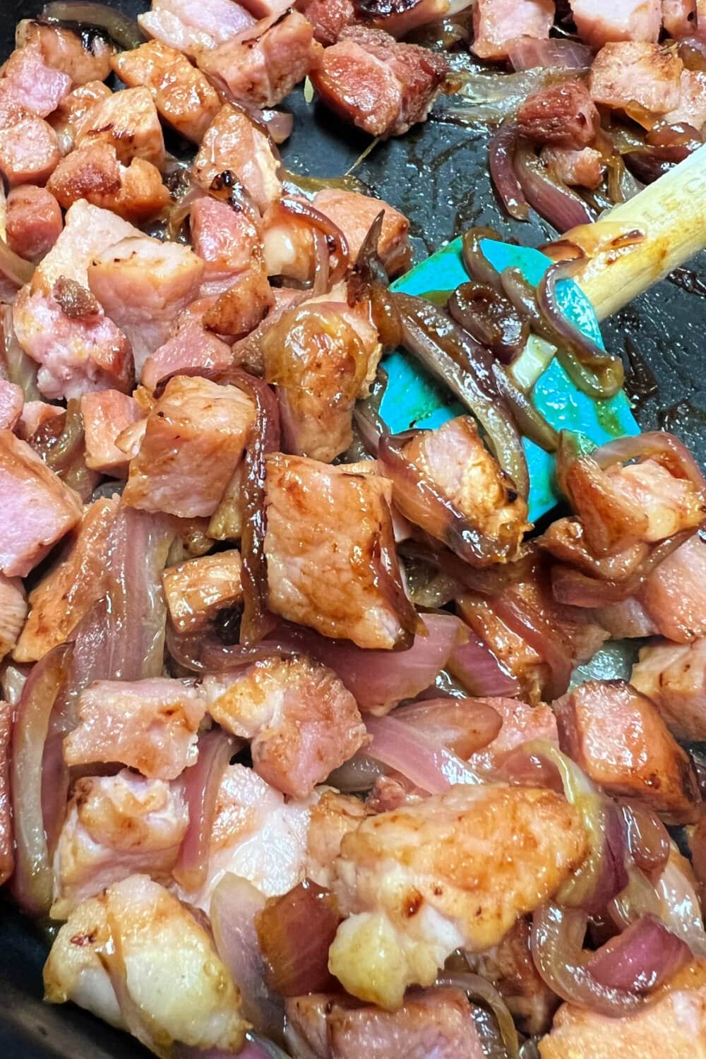 Caramelized onions and ham steak pieces in a hot skillet. 