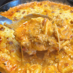 A big spoonful of creamy baked tortellini with meat sauce.
