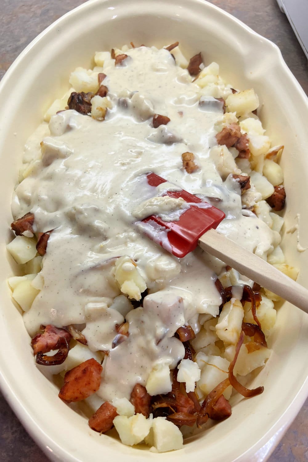 A baking dish full of potatoes and ham with a white sauce over the top. 