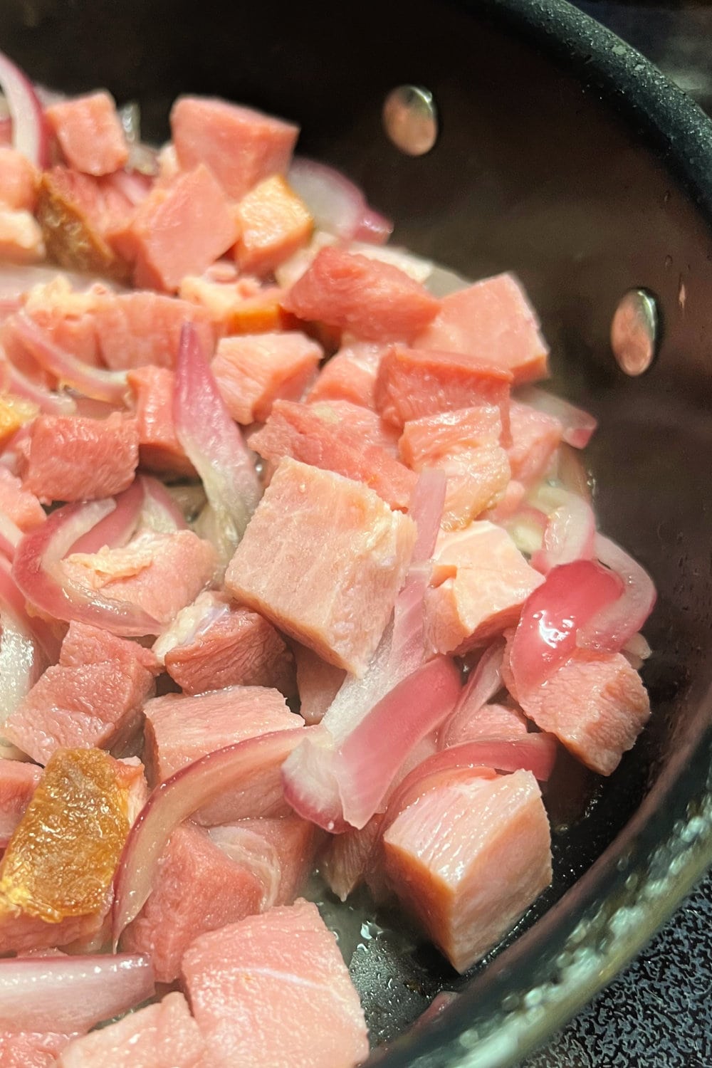 Ham steak and onions placed into a skillet to brown.