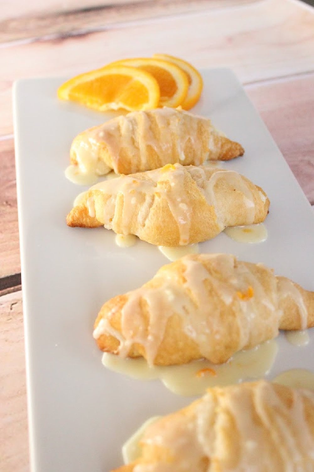 Orange breakfast crescent rolls with icing on a white plate with an orange