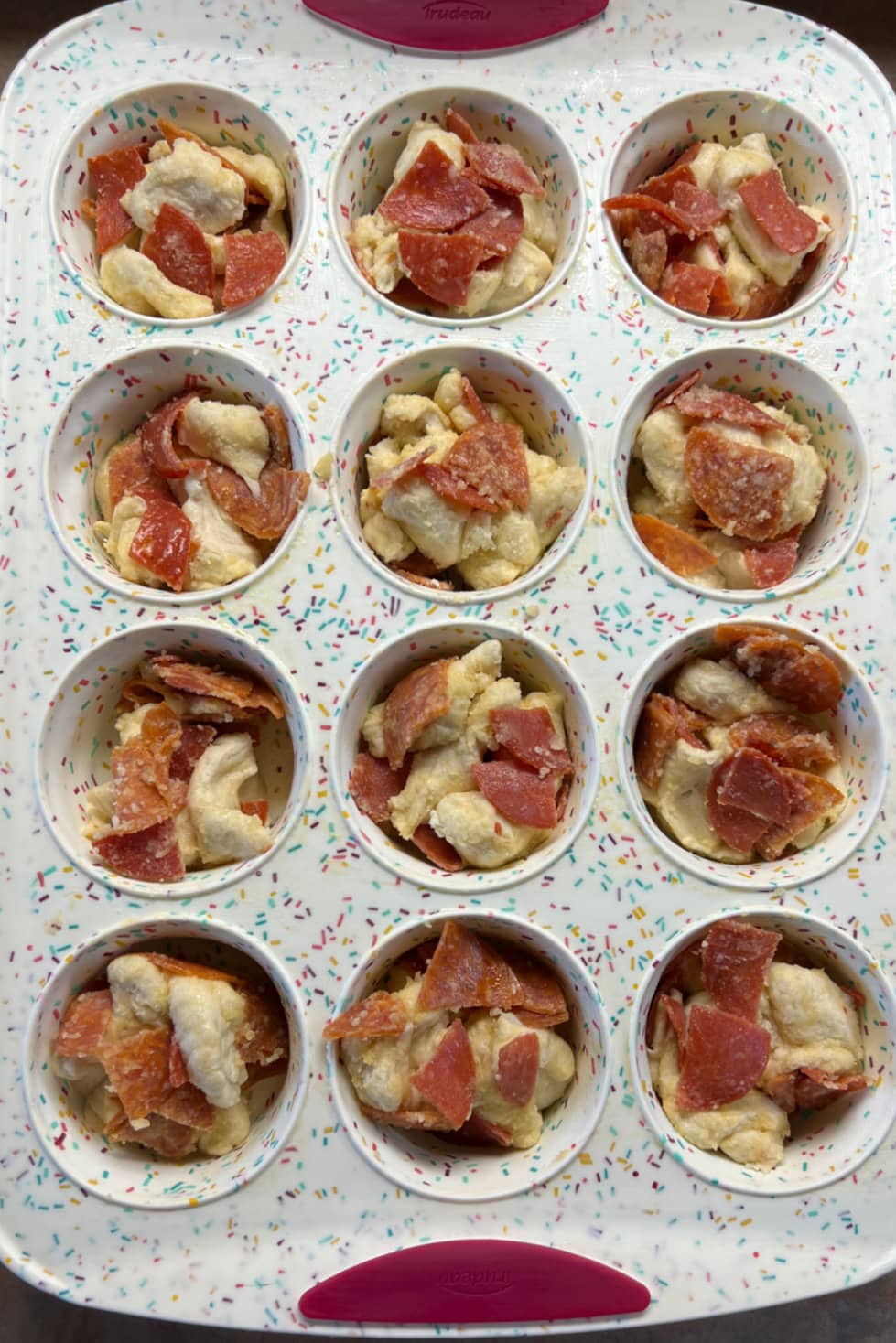 Ready for the oven, twelve Pepperoni Biscuit Bites in a muffin tin. 