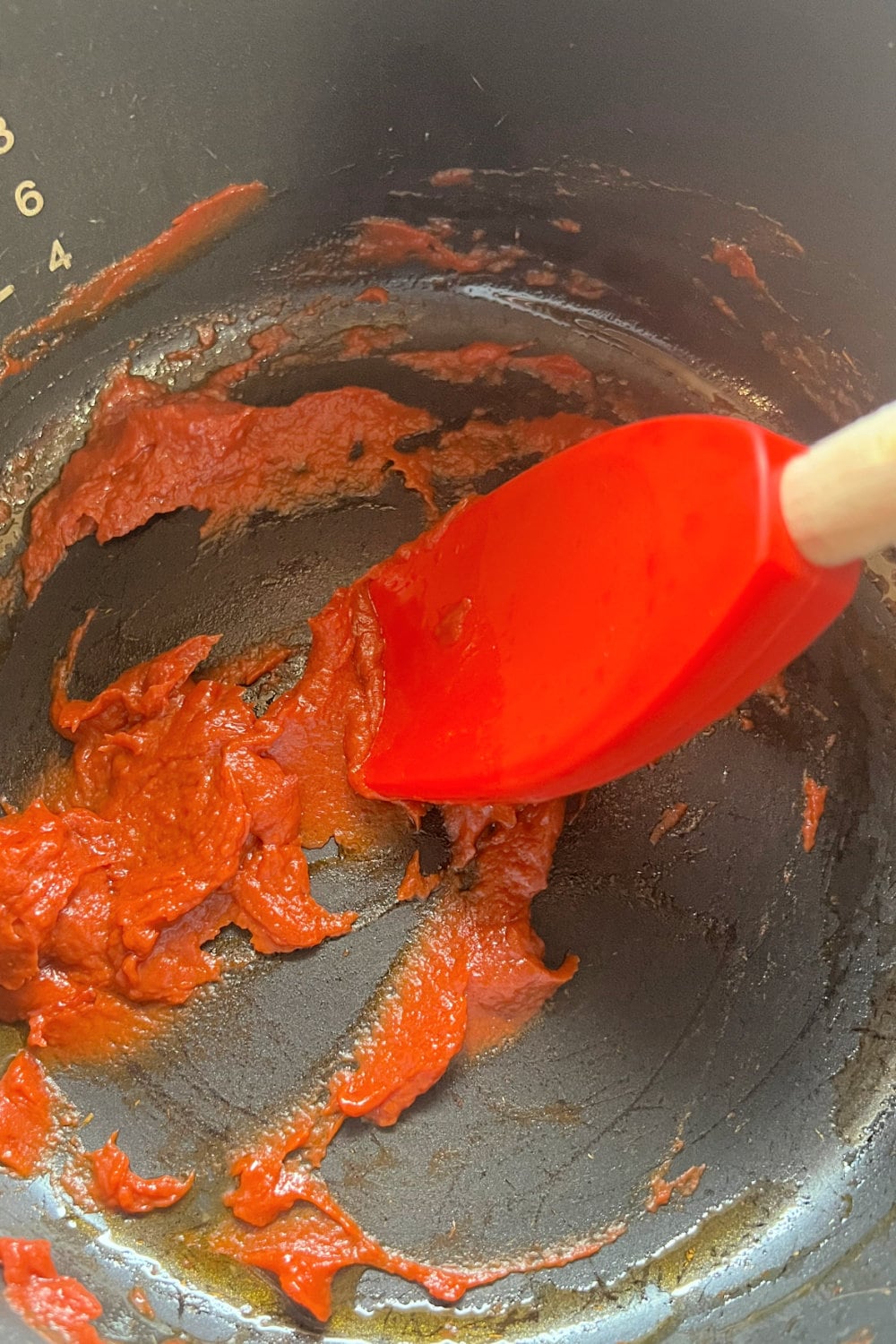 Bright red tomato paste added to a pot for making a sauce. 