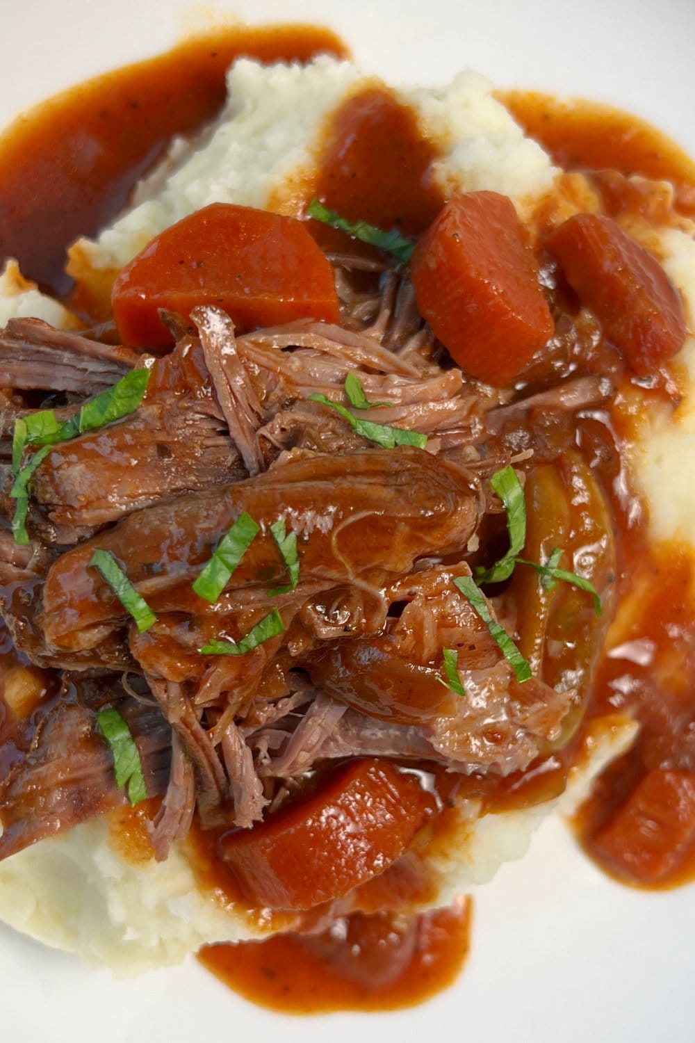 A serving of chuck tender roast shredded over mashed potatoes with gravy. 
