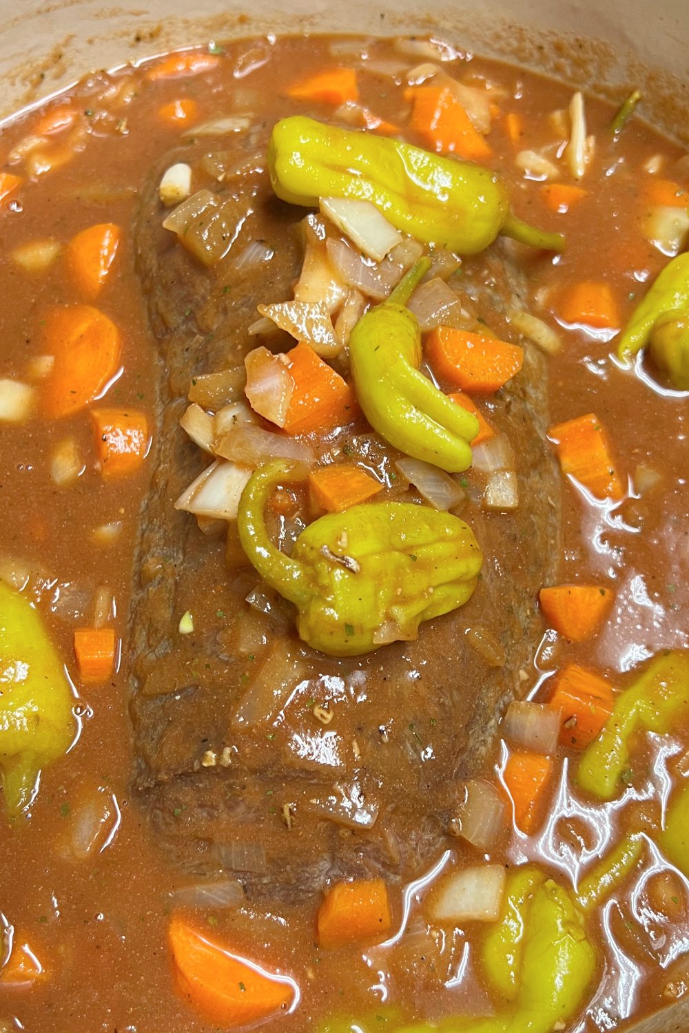 Chuck tender roast nearly submerged in the gravy and aromatics in a pot. 