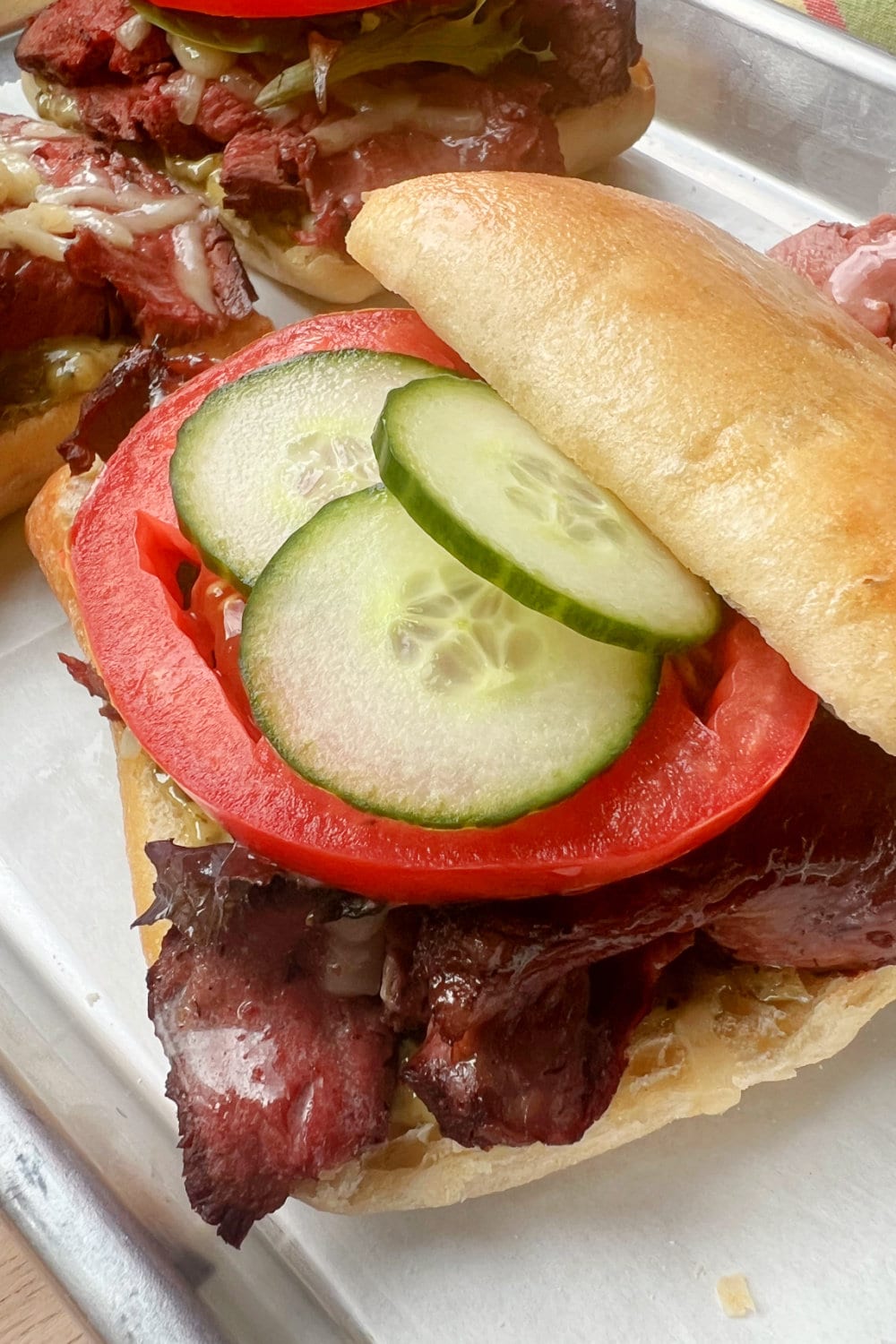 A Beef Tenderloin Sandwich topped with tomato and cucumbers. 
