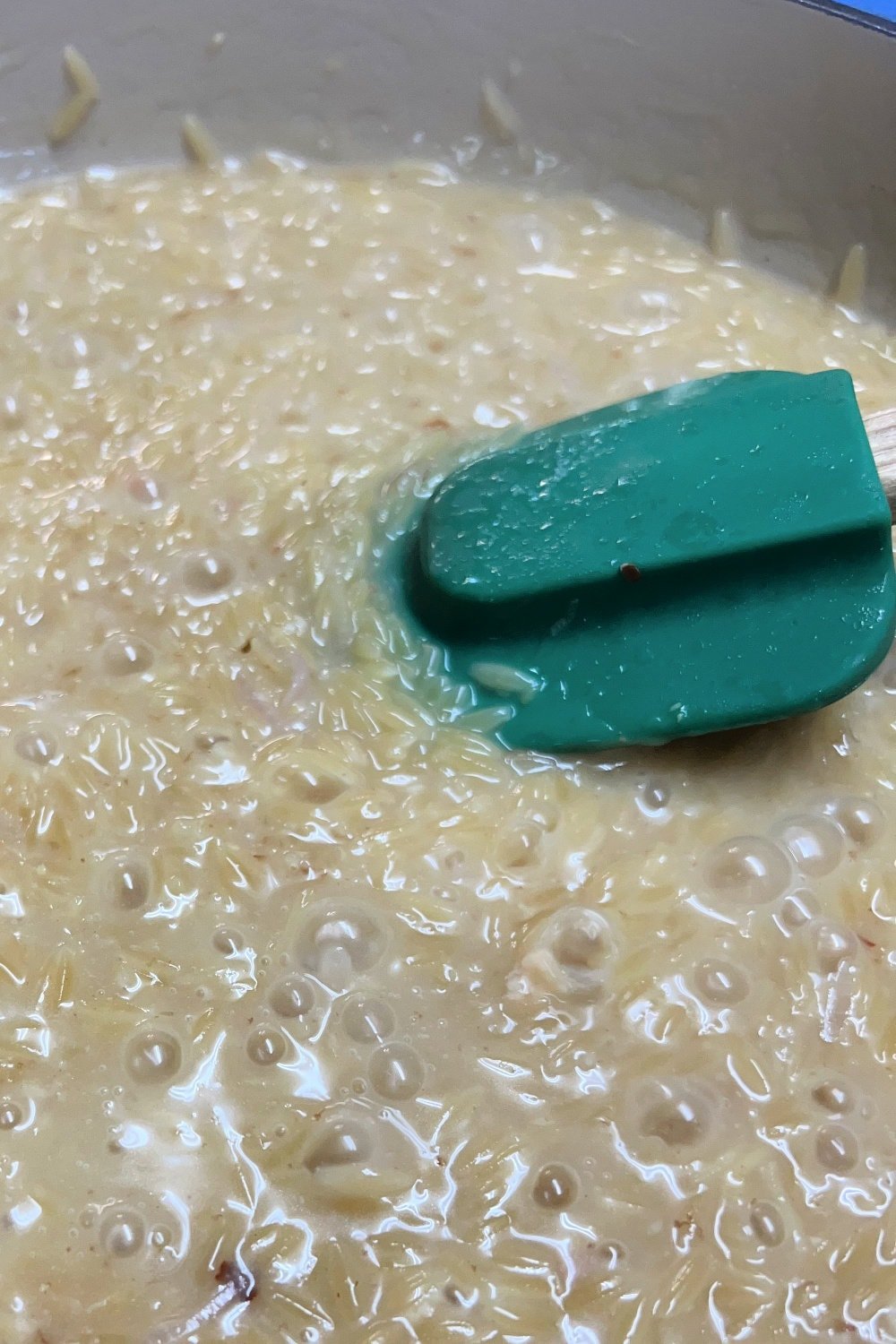 Orzo simmering in a skillet with chicken broth. 