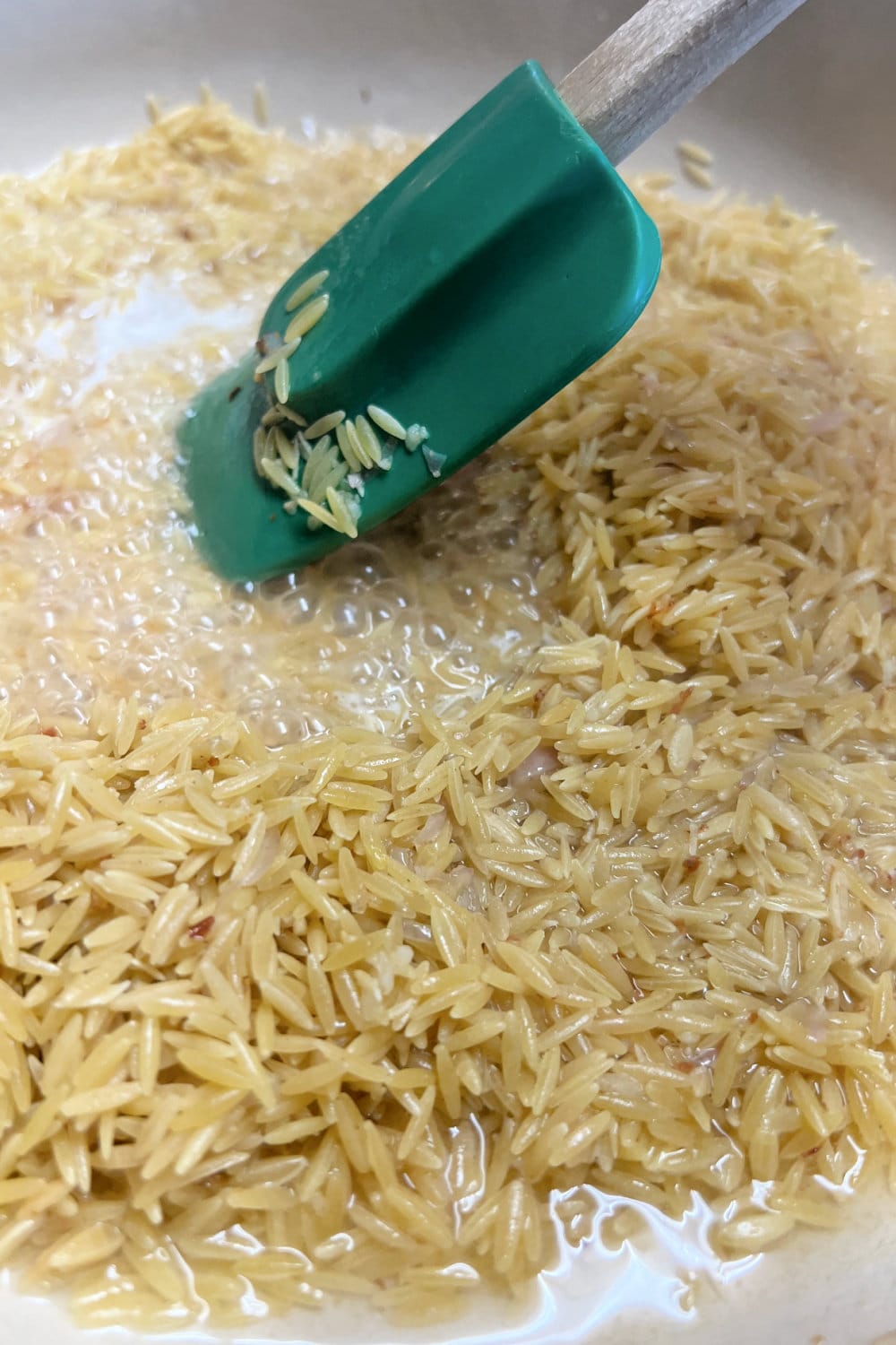 Deglazing a skillet of orzo with lemon juice and wine. 