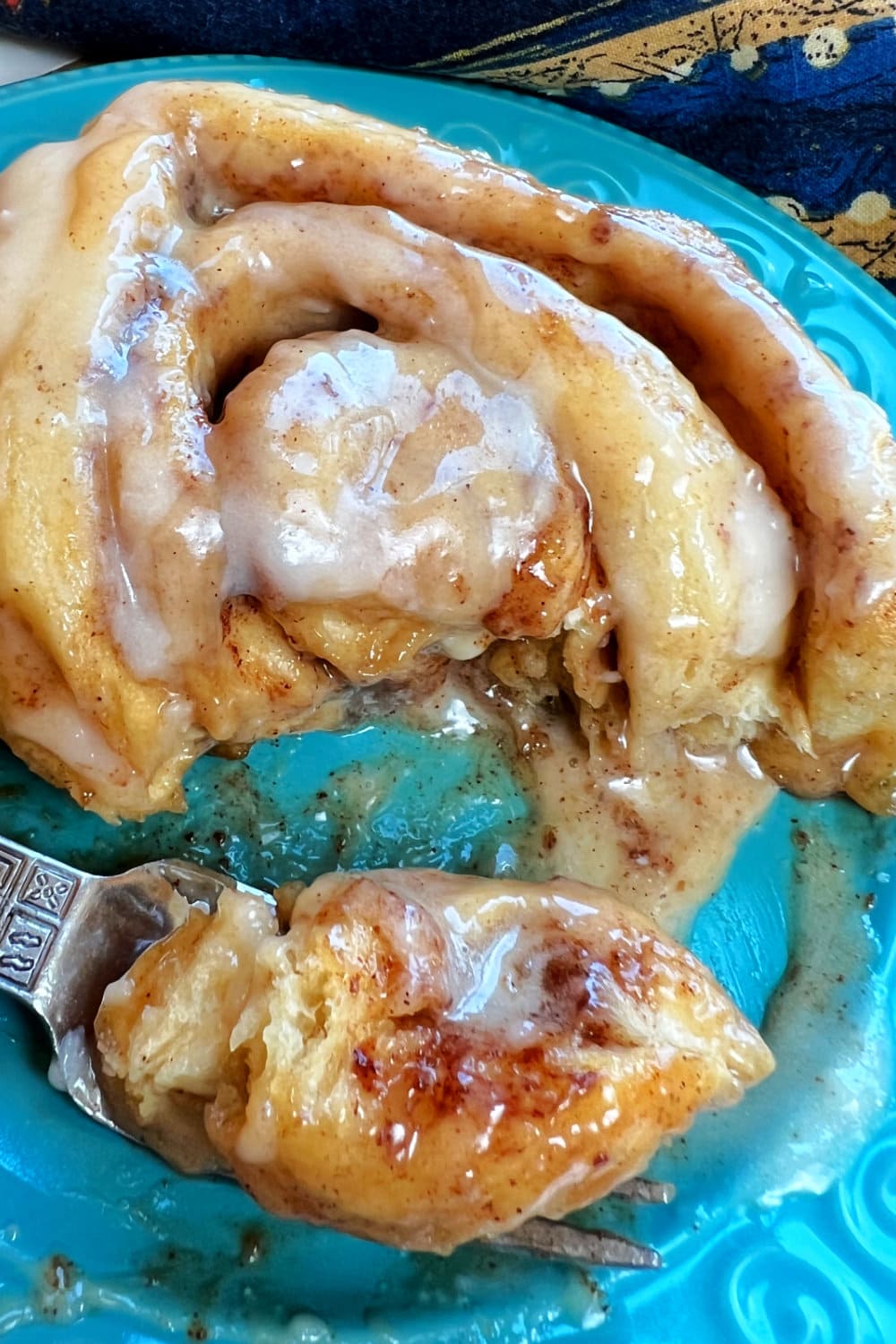 A fresh cinnamon roll with bite on a fork. 