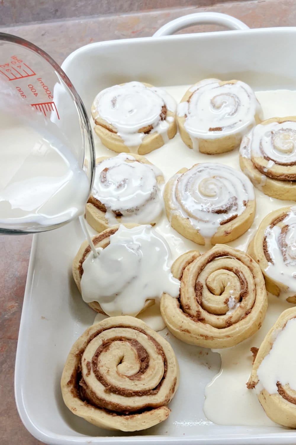 Pouring heavy whipping cream over the cinnamon rolls in the baking dish. 