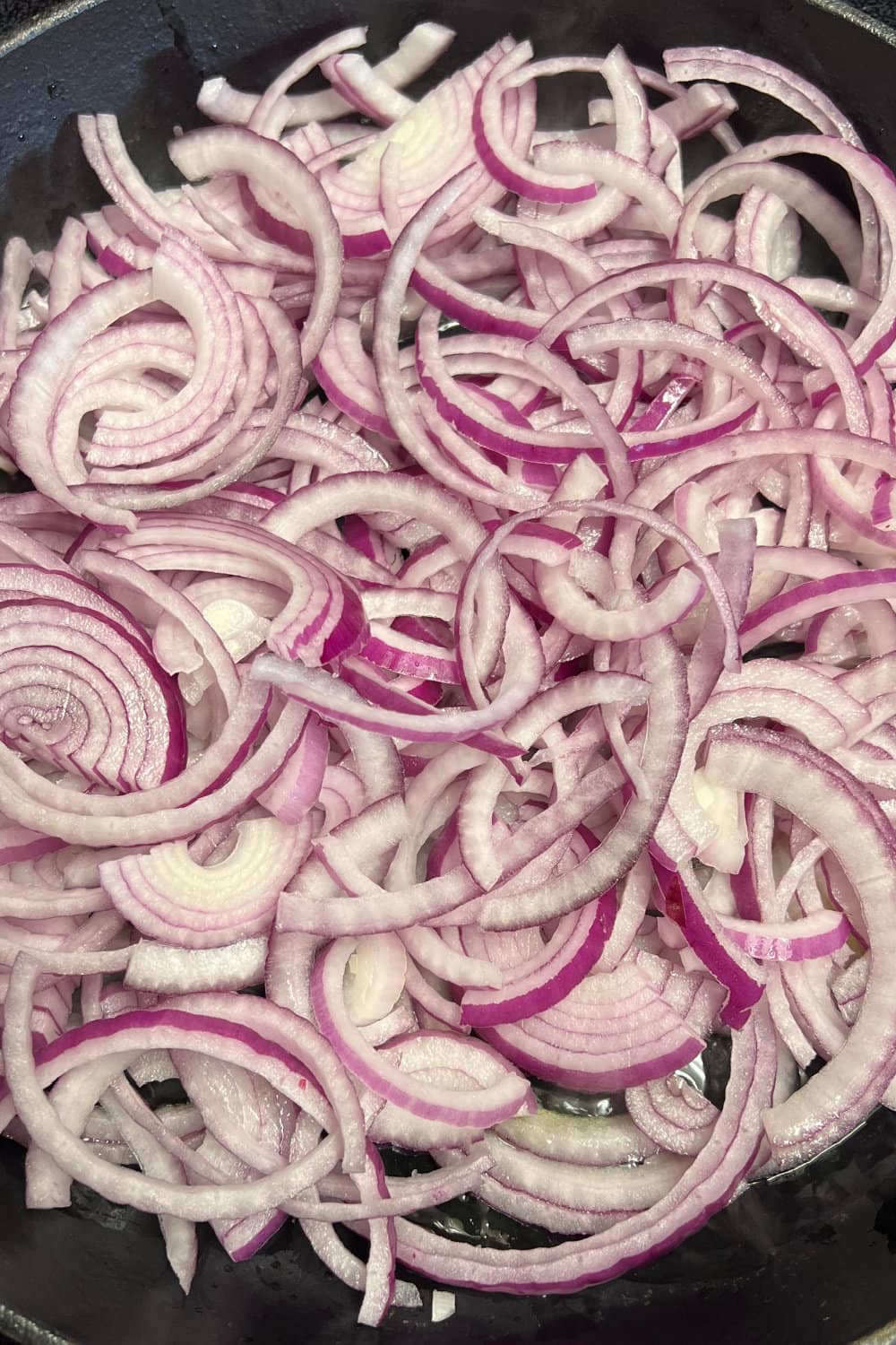 Raw sliced red onions in a skillet. 