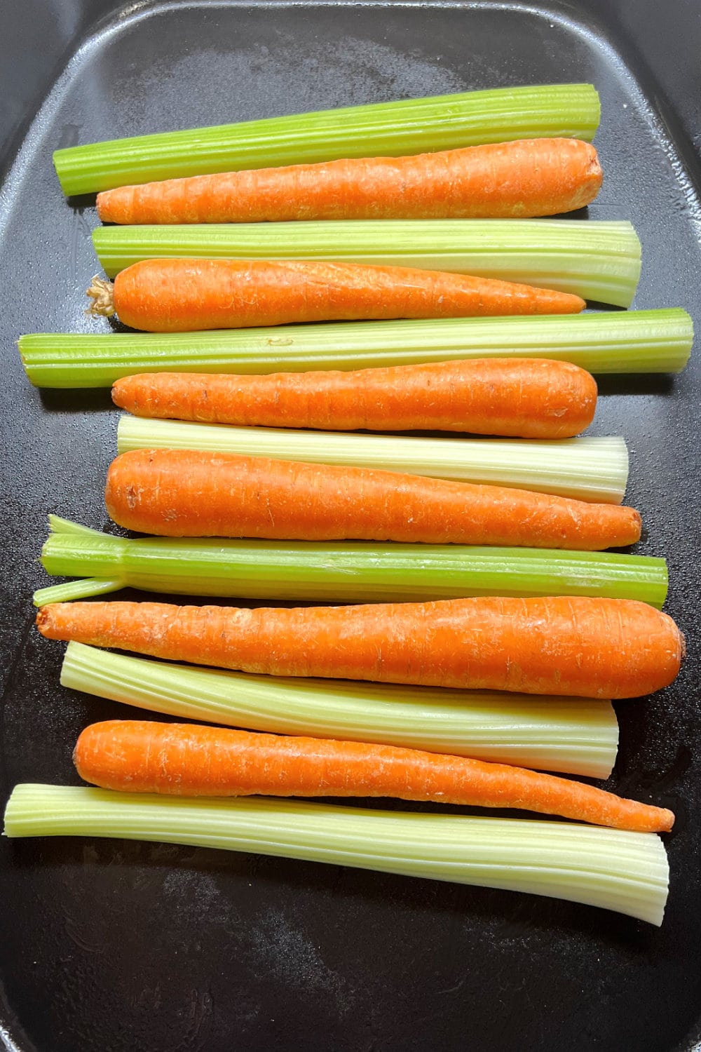 Whole carrots and ribs of celery side-by-side in a roaster.