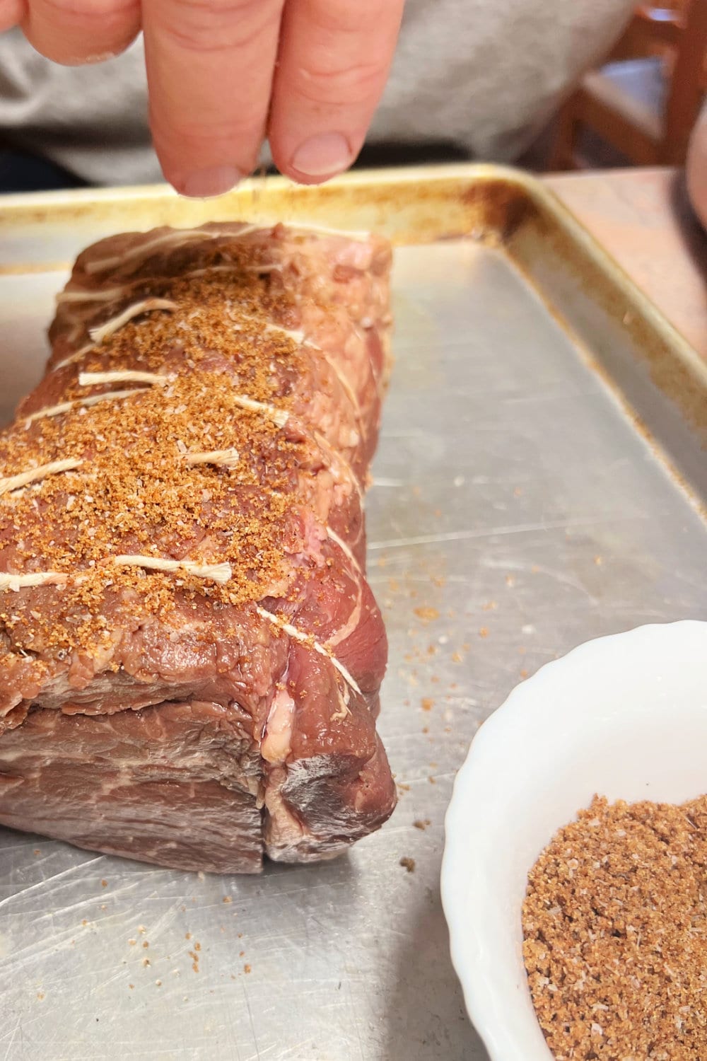 Applying dry rub to a tied beef tenderloin on a baking sheet. 