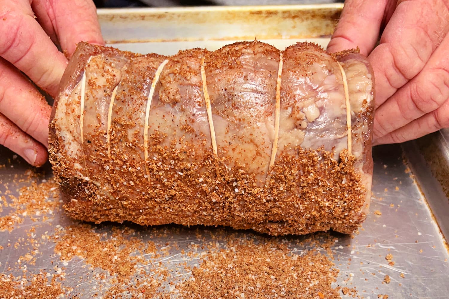 Rolling a tied beef tenderloin in dry rub on baking sheet. 