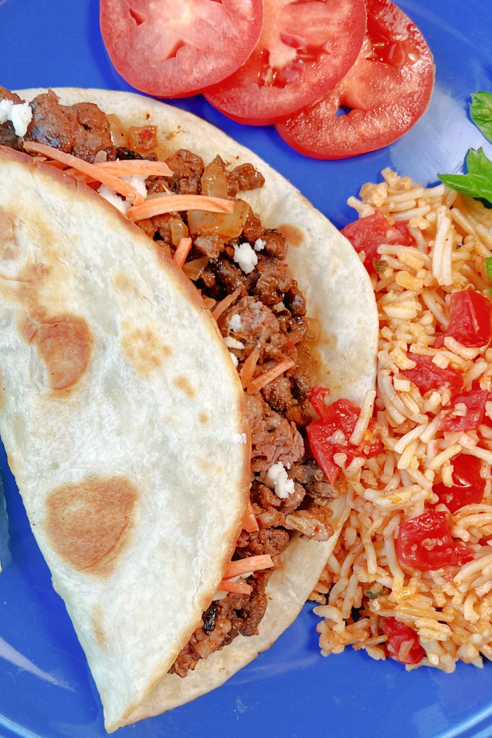 A warm Carne PIcada Taco on a blue plate with rice on the side. 