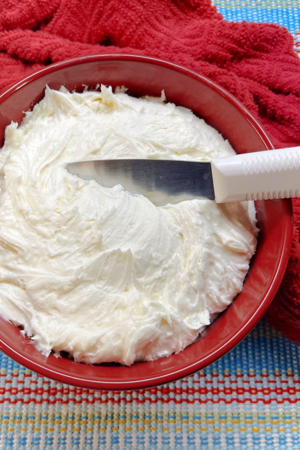 A red bowl of cinnamon roll frosting with a spreader. 