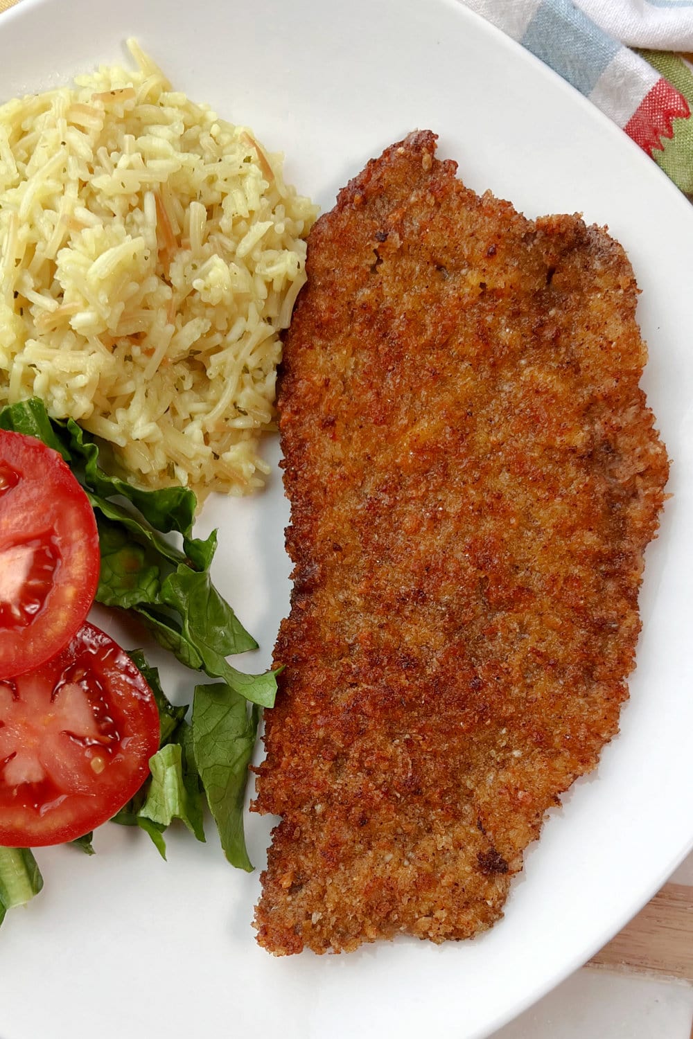 Milanesa Steak with rice and mixed greens on a white plate. 