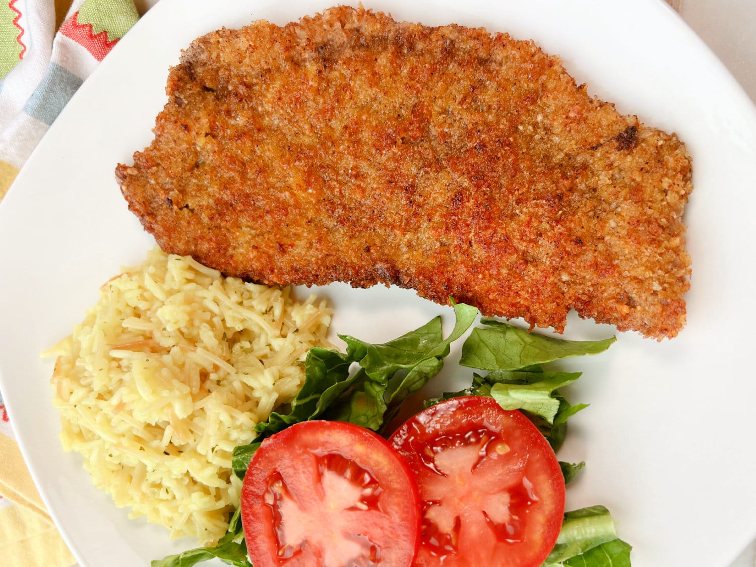 Golden brown and crispy, Steak Milanesa on a white plate with rice on the side. 